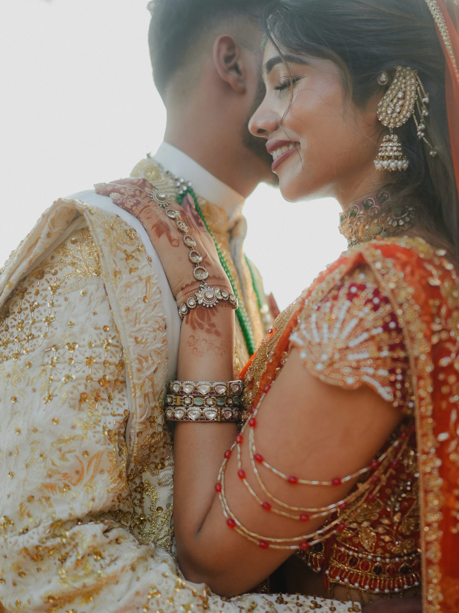 A bride in heavy bridal jewellery beside her groom, both close-up