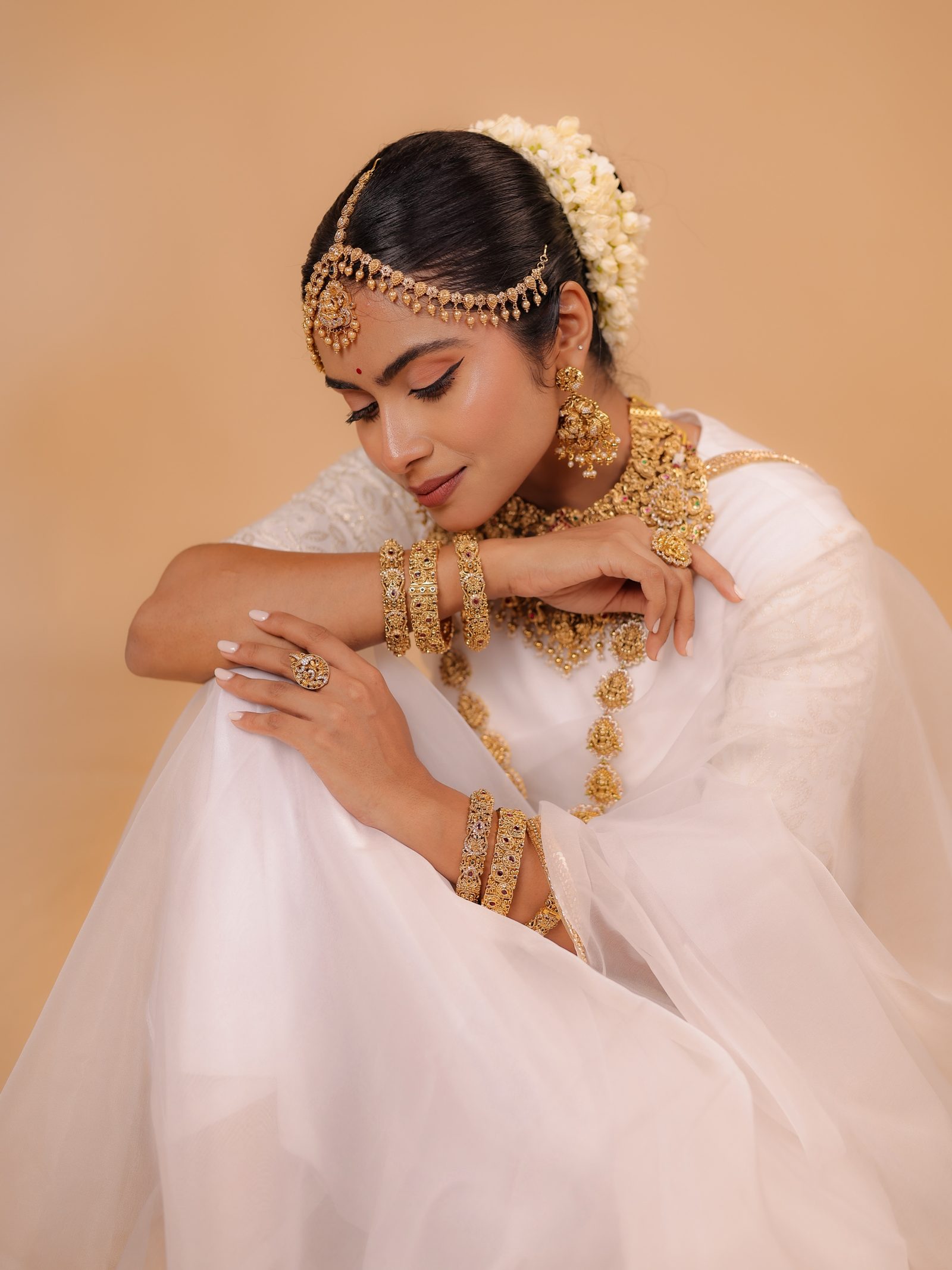 A bride in white kasavu wearing layered gold temple naga jewellery